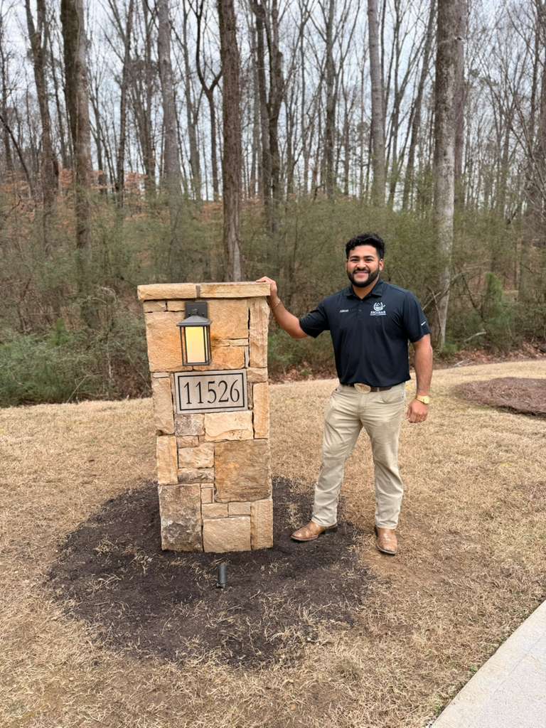 Adrian of Escobar Masonry beside a custom stone pillar with address plaque